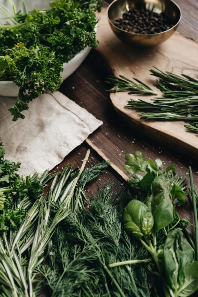 A variety of fresh herbs including rosemary, dill, and basil arranged on a wooden board for culinary use.